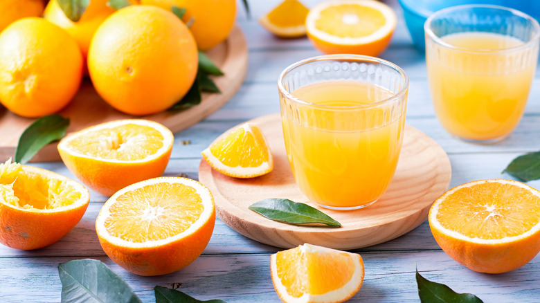 glass of orange juice surrounded by oranges