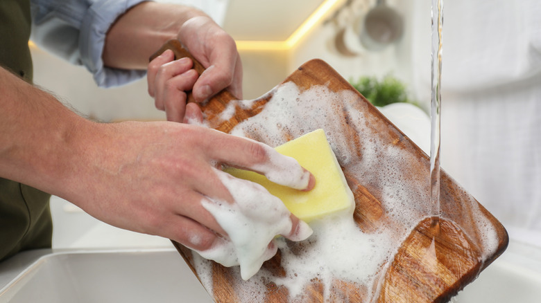 Man cleaning wooden cutting board at kitchen sink