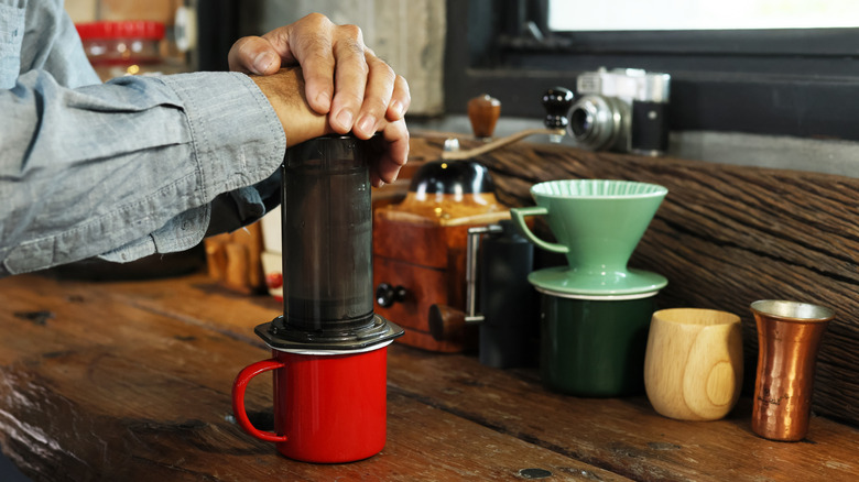 A men presses on an AeroPress sitting on top of a small red coffee cup