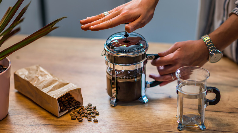 A hand pressing the plunger on a French press next to an open bag of coffee