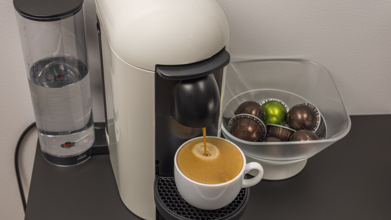 An automatic coffee machine brewing coffee next to a bowl of pods