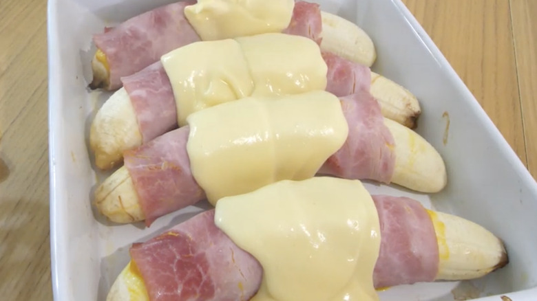 a casserole dish holding four ham-wrapped bananas covered in hollandaise