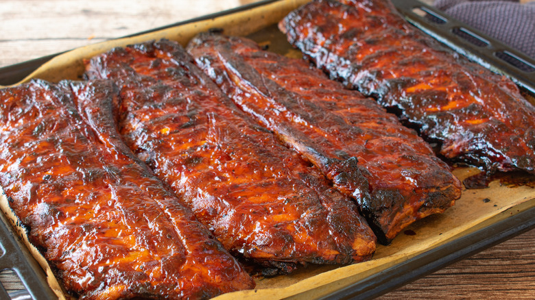 Close-up of a sheet pan with charred crispy ribs and barbecue sauce