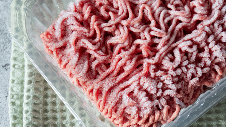 A package of ground beef in a clear plastic container ontop of a cloth