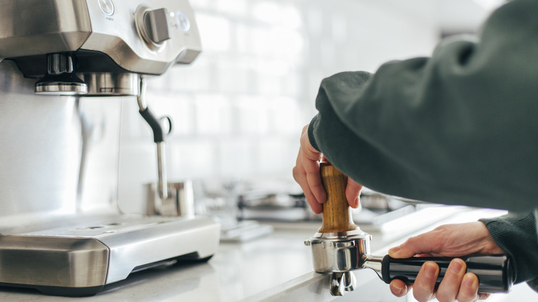 hands tamping down ground espresso beans into a portafilter