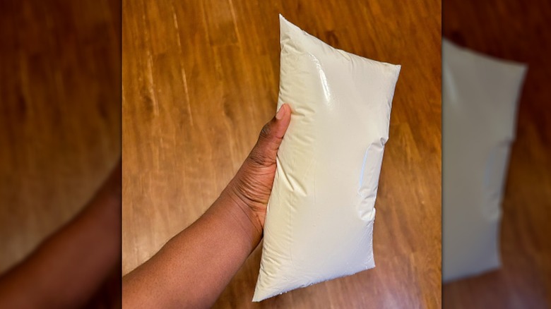 A hand holding a single bag of milk