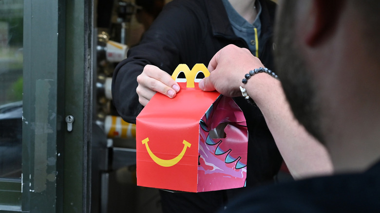 Someone grabbing a red Happy Meal box from a drive-thru window