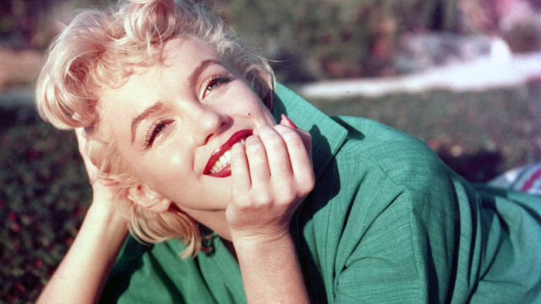 A close up of Marilyn Monroe lying down with her head propped on her hand smiling