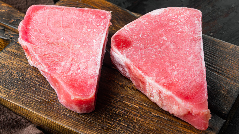 Frozen tuna steaks on wooden board