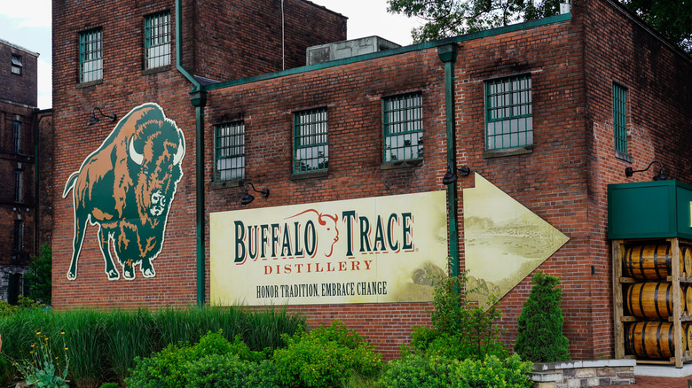 a brick building with a large Buffalo Trace logo on the side and a rack of oak barrels beside it