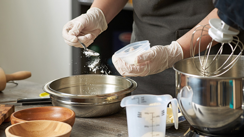 baker adding baking powder to a mixing bowl