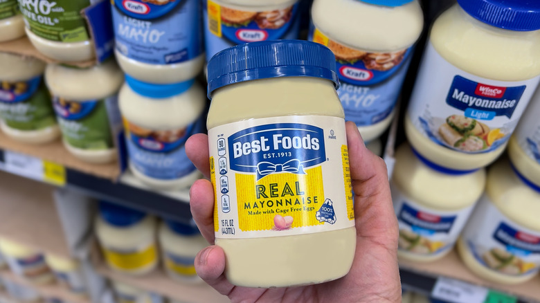 A person holds up a jar of Best Foods mayo in a grocery store