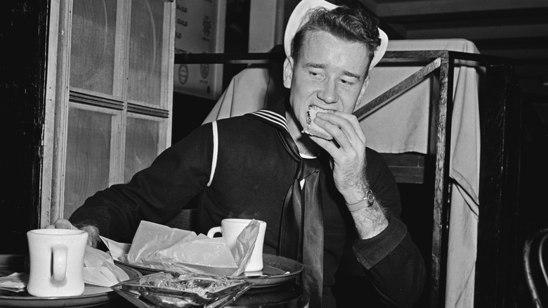 Vintage photo of US Navy sailor eating with coffee cup on a table in front of him.