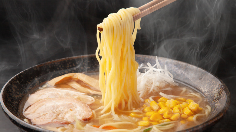 Chopsticks pulling ramen noodles from a steaming bowl