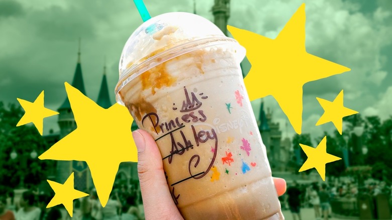 Hand holding a Disney-themed Starbucks drink with stars and Disneyland in the background