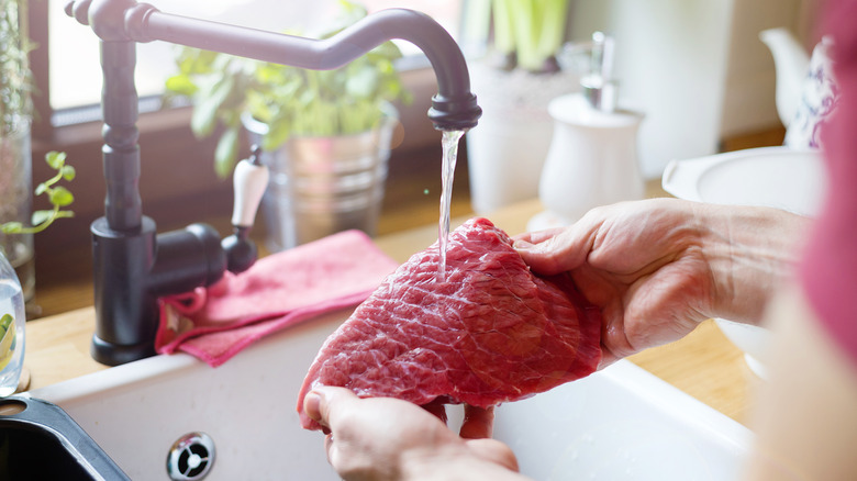 hands rinsing raw steak