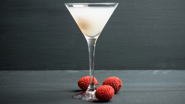 A milky-colored lychee martini alongside fresh, red, unpeeled lychees