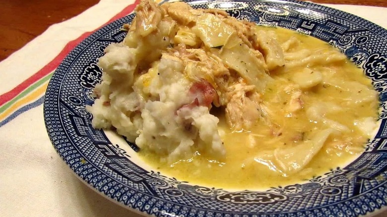 A blue-rimmed plate loaded with chicken and noodles in gravy over mashed potatoes.