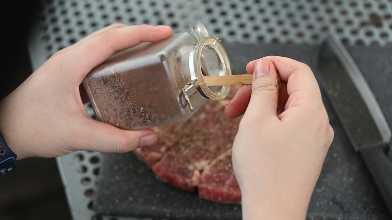Person sprinkling seasoning on steak