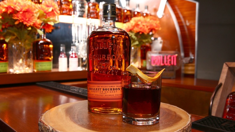 A bottle of Bulleit bourbon next to a Revolver cocktail
