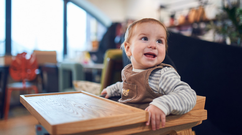 A baby smiles from a high chair in a restaurant