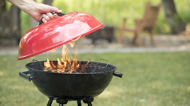 Someone lifting the top off a flaming charcoal grill