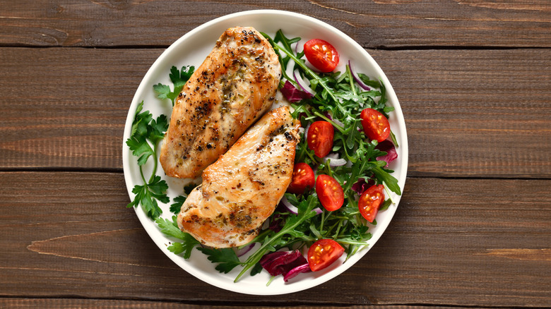 two baked chicken breasts on a plate with a fresh salad