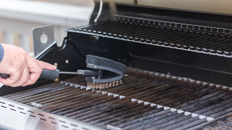 A person using a stainless steel brush to clean off grill grates prior to using a gas grill