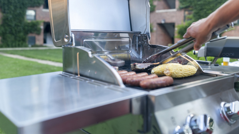 A close-up view of a man using tongs to turn pieces of meat on an open gas grill