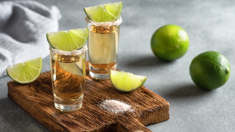 Two shots of tequila with limes and salt on a wooden board