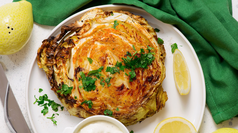 Cabbage steak on plate with an herb garnish, lemon wedges, and sauce