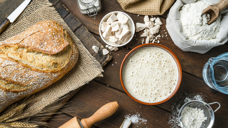 ingredients for homemade bread and a fresh loaf on a board all laid out on a table