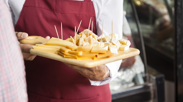 A person serves samples of cheese on a wooden board.