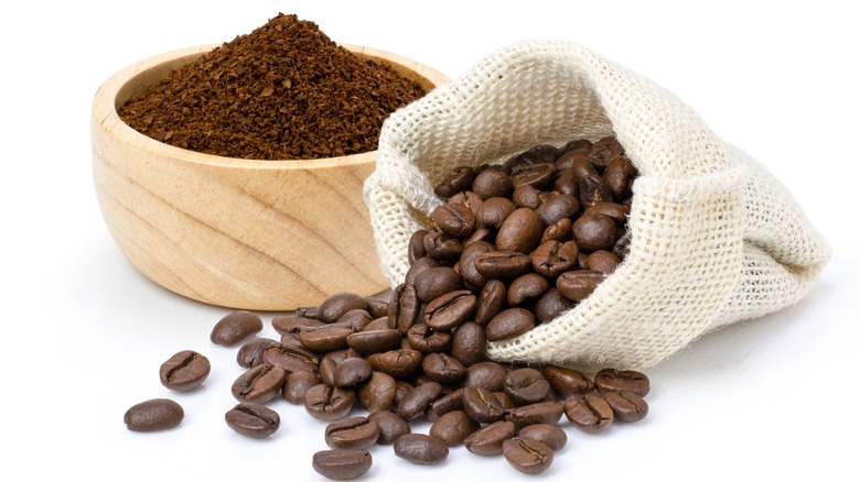 Coffee beans in a sack next to a bowl of ground coffee
