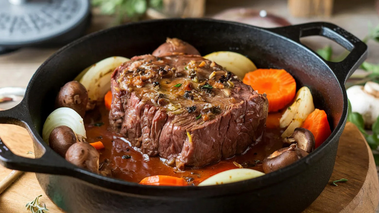 Pot roast cooking in a liquid with onions and carrots