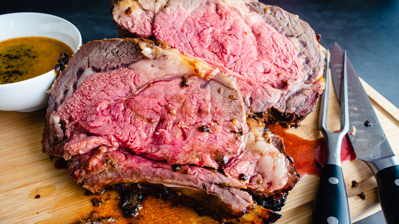 Slices of rare prime rib next to tools and bowl of jus