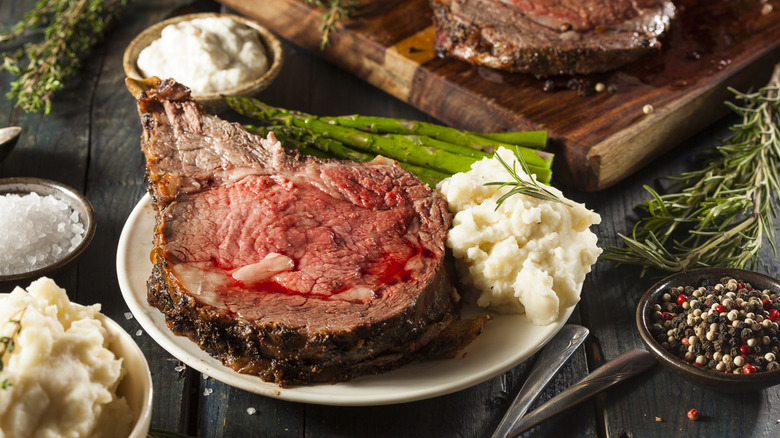 Slice of prime rib on plate next to mashed potatoes and asparagus