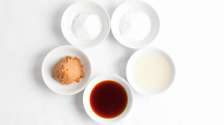 five white bowls containing sugar, salt, vinegar, soy sauce, and miso