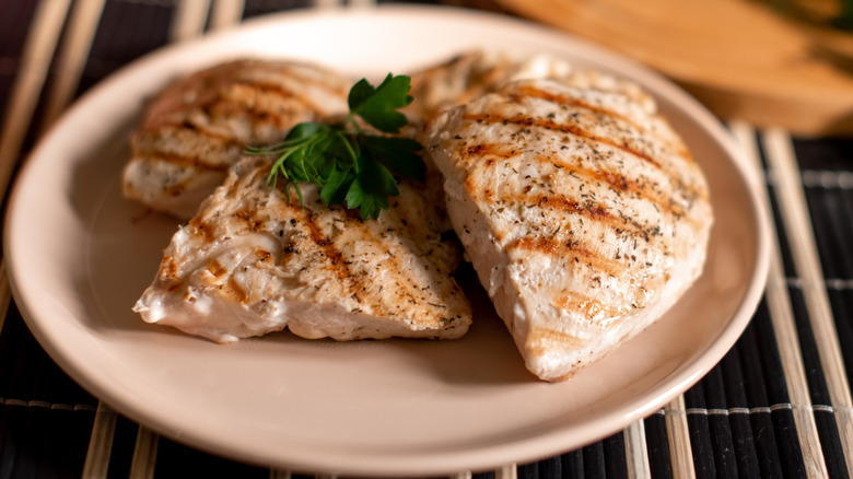 Grilled chicken breast with garnish, on a pink plate