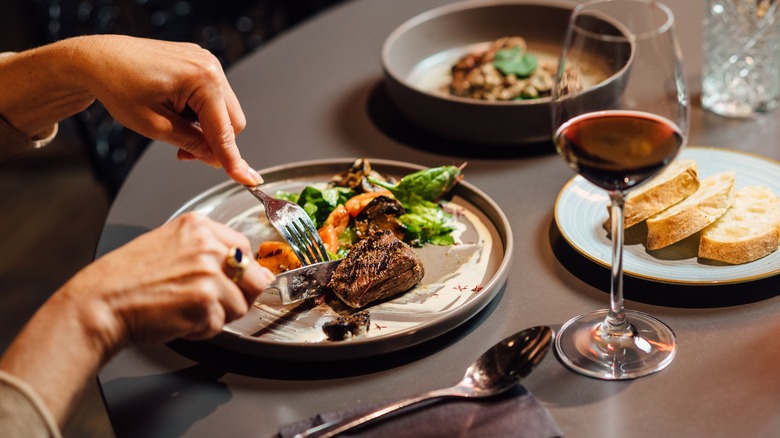 Person eating a meal at a restaurant with red wine on the side