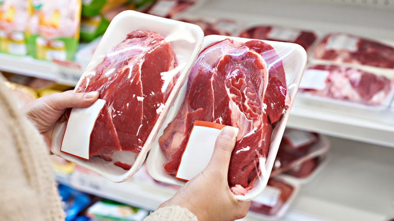 A person holds two packages of red meat