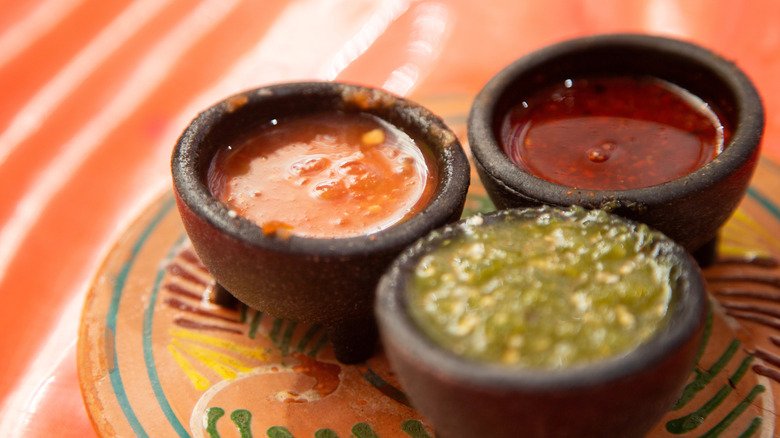 Three small black bowls of different salsas on a clay dish