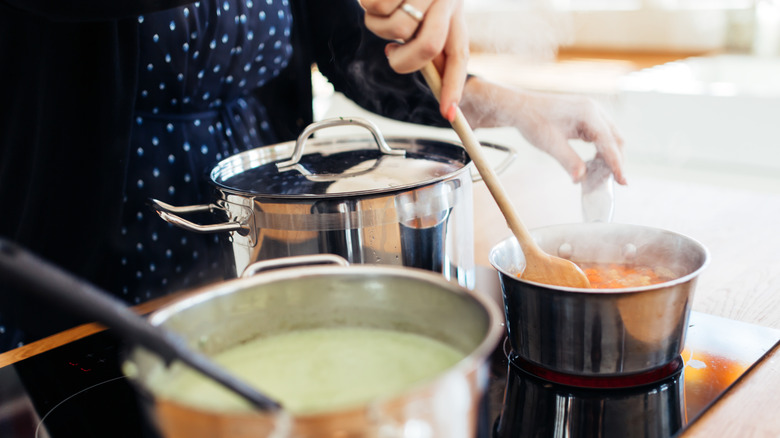 person cooking a couple pots of soup on stove