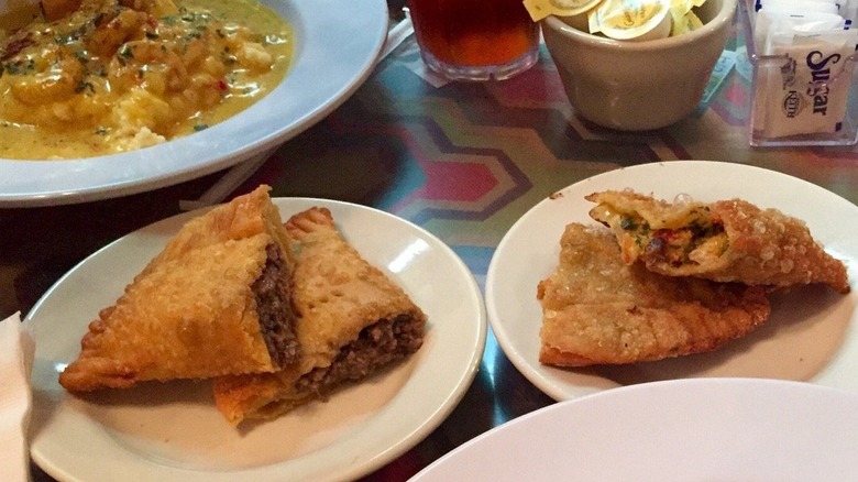 A Natchitoches meat pie from Lasyones Meat Pie Restaurant that's split in half on a plate next to other food
