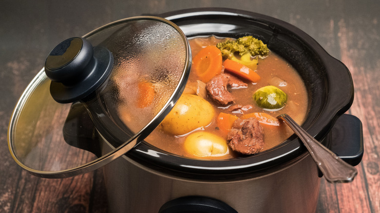 Slow cooker filled with beef, broth, vegetables, and potatoes