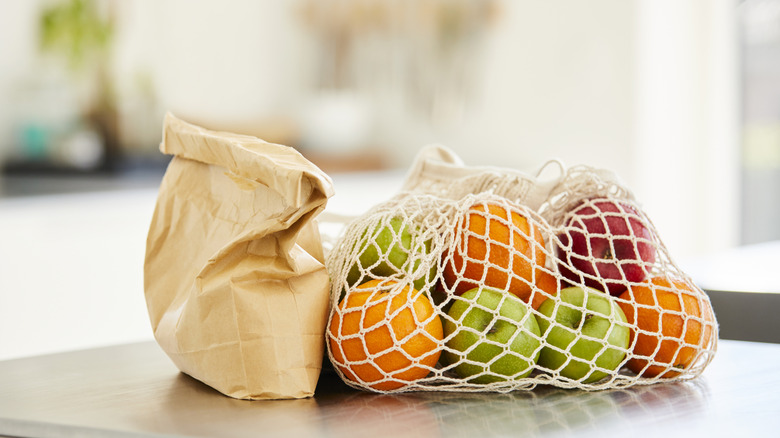 A paper bag and a string bag full of fruit on a metal table