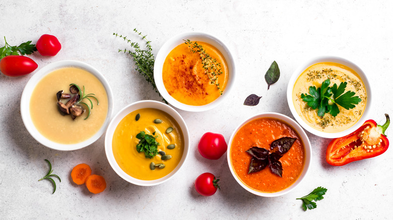 Bowls of colorful, creamy soups against white background