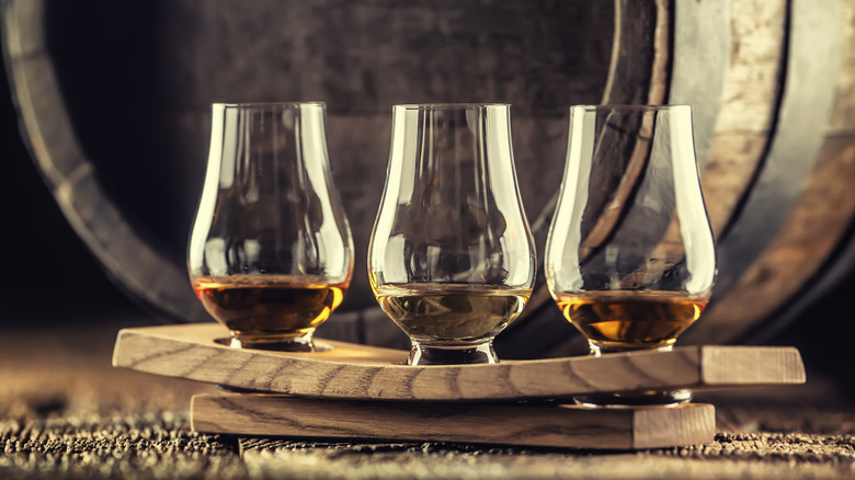 3 Glencairn glasses of whisky set out for tasting in front of barrel