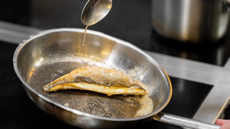 fish searing in stainless steel pan