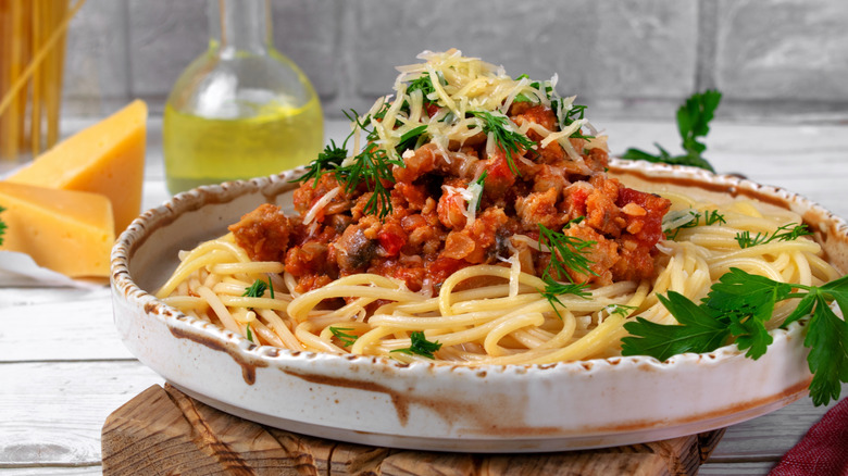 Seafood bolognese served over spaghetti on rusted white rimmed plate with cheese and olive oil bottle in background